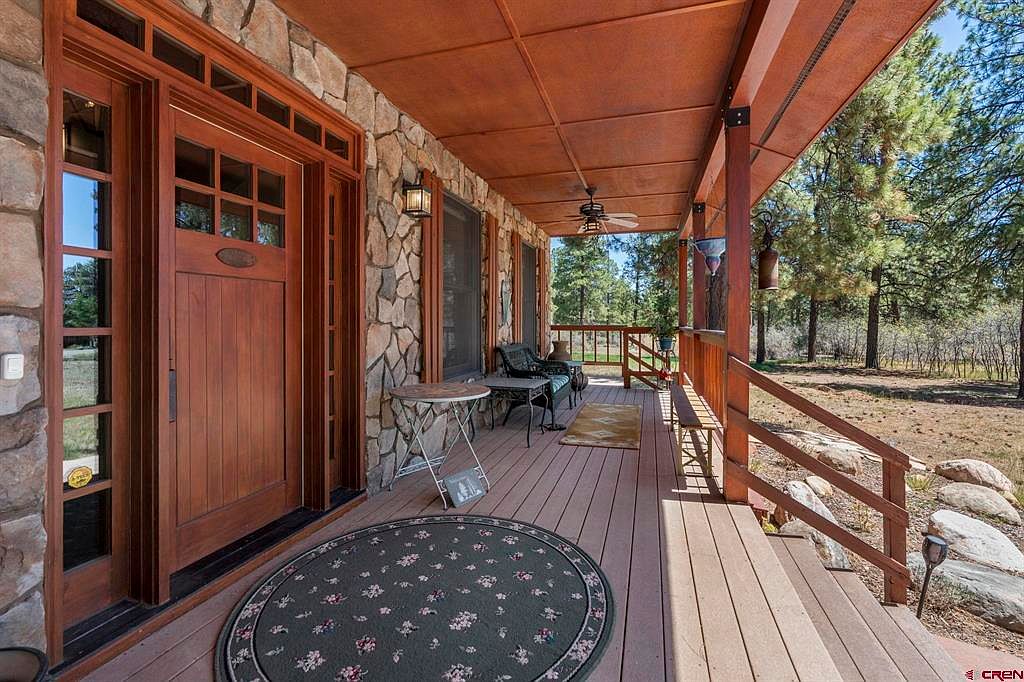 Front porch entry with stone walls, custom cherry door with glass transoms, and a bistro table looking out to the pine forest